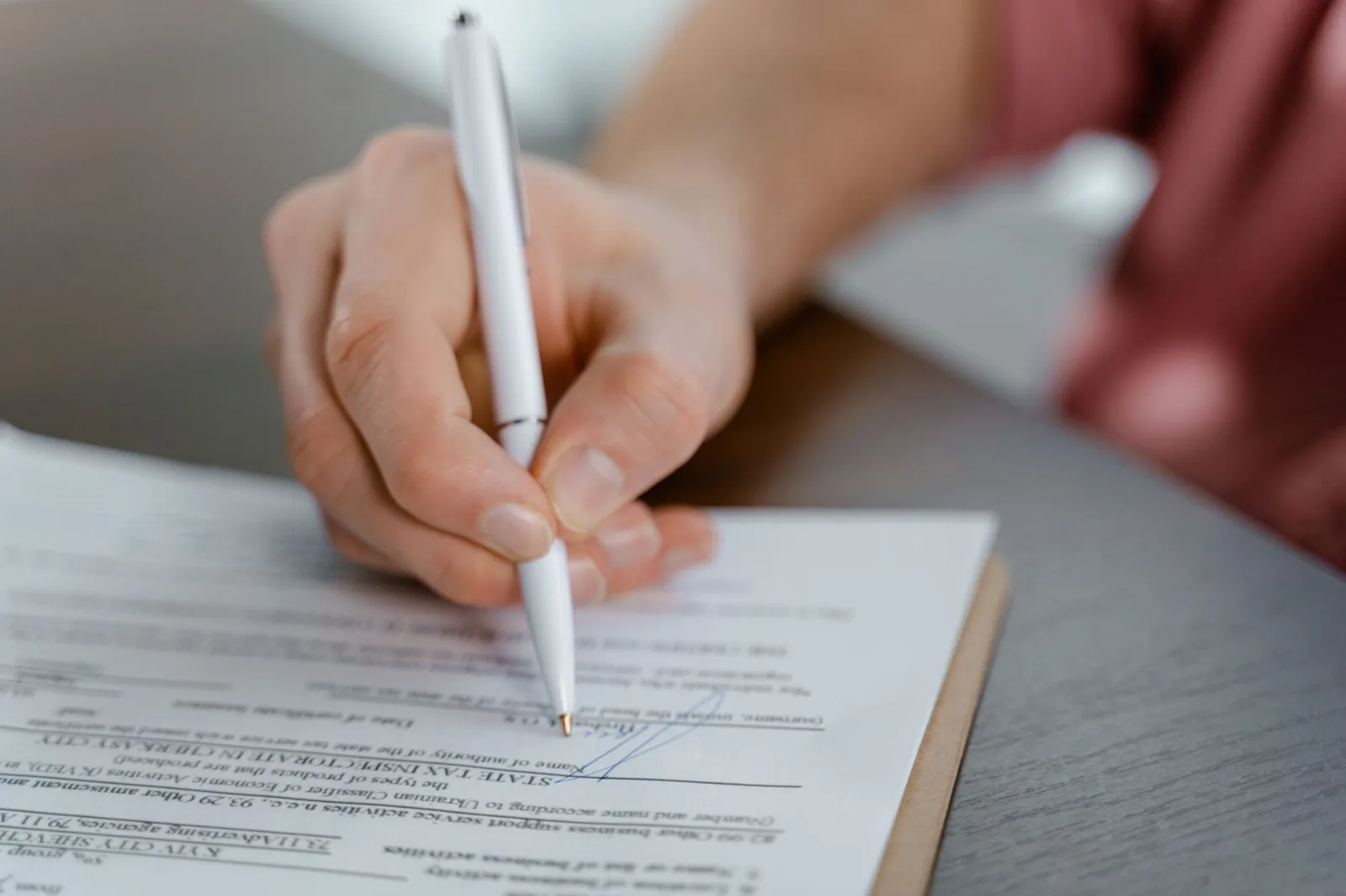 Detailed view of a hand writing a signature on an official document with a ballpoint pen.